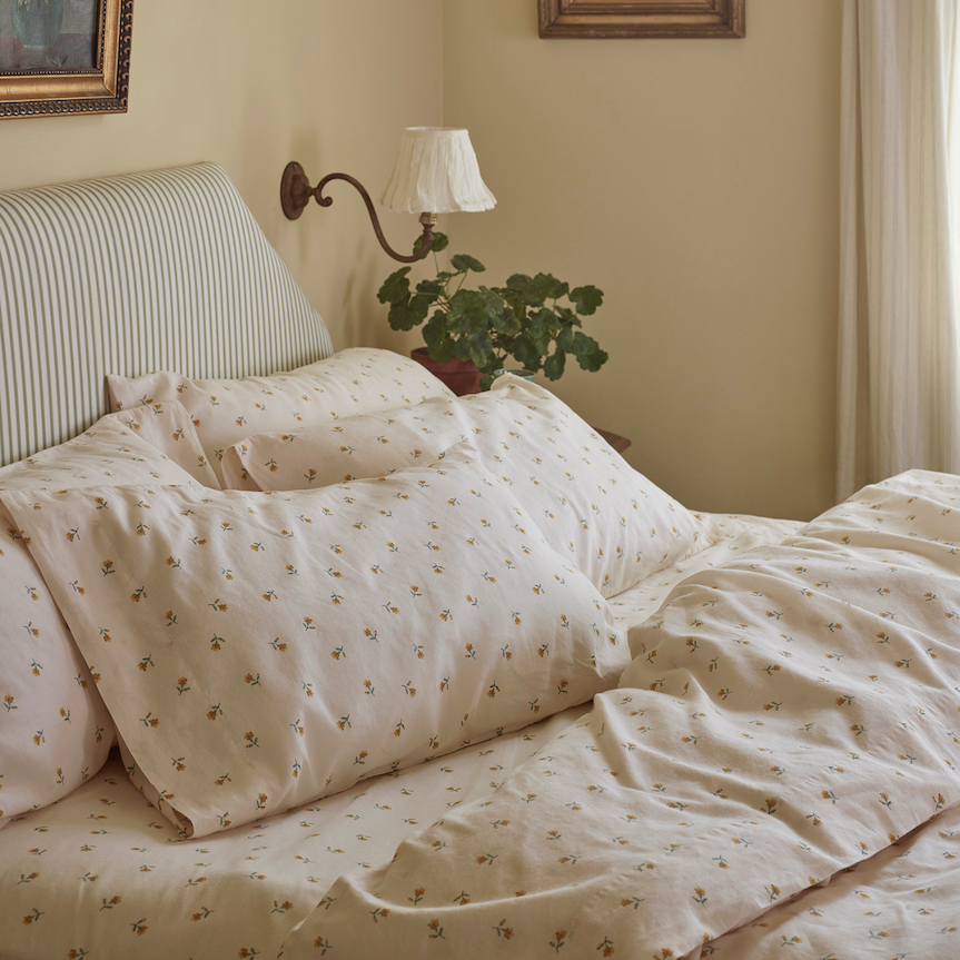 Image of an unmade bed with a flower bud, white bedding in an off-white bedroom.