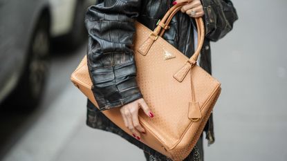 Woman wearing a glossy manicure holding a Prada tote bag
