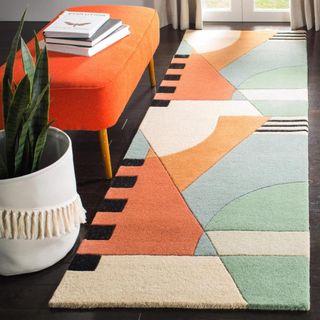 An abstract runner rug in orange, green, blue, red and black sits on a black floor