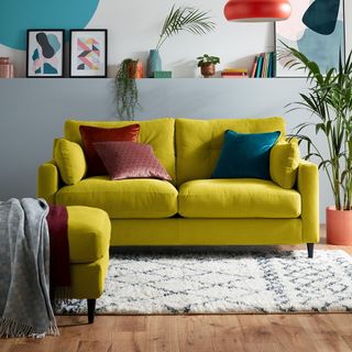 Mustard coloured sofa in a blue living room with wooden floors and cream rug