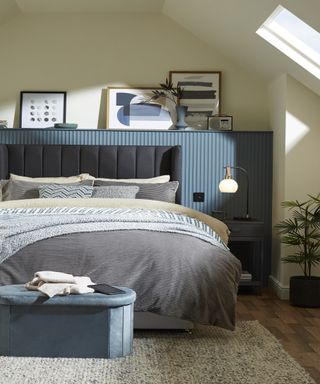 Loft bedroom with double bed with upholstered headboard, blue painted shelf behind and wood floor with neutral rug