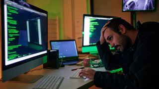 A person at a computer looking dejected with one hand on their head staring at computer code