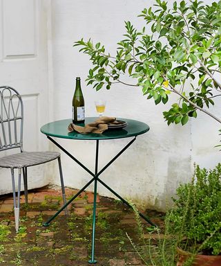 A green folding galvanized iron dining table in outdoor courtyard with bottle of wine