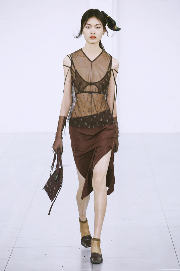 Model wears cream sheer top with sequins and intricate bra
