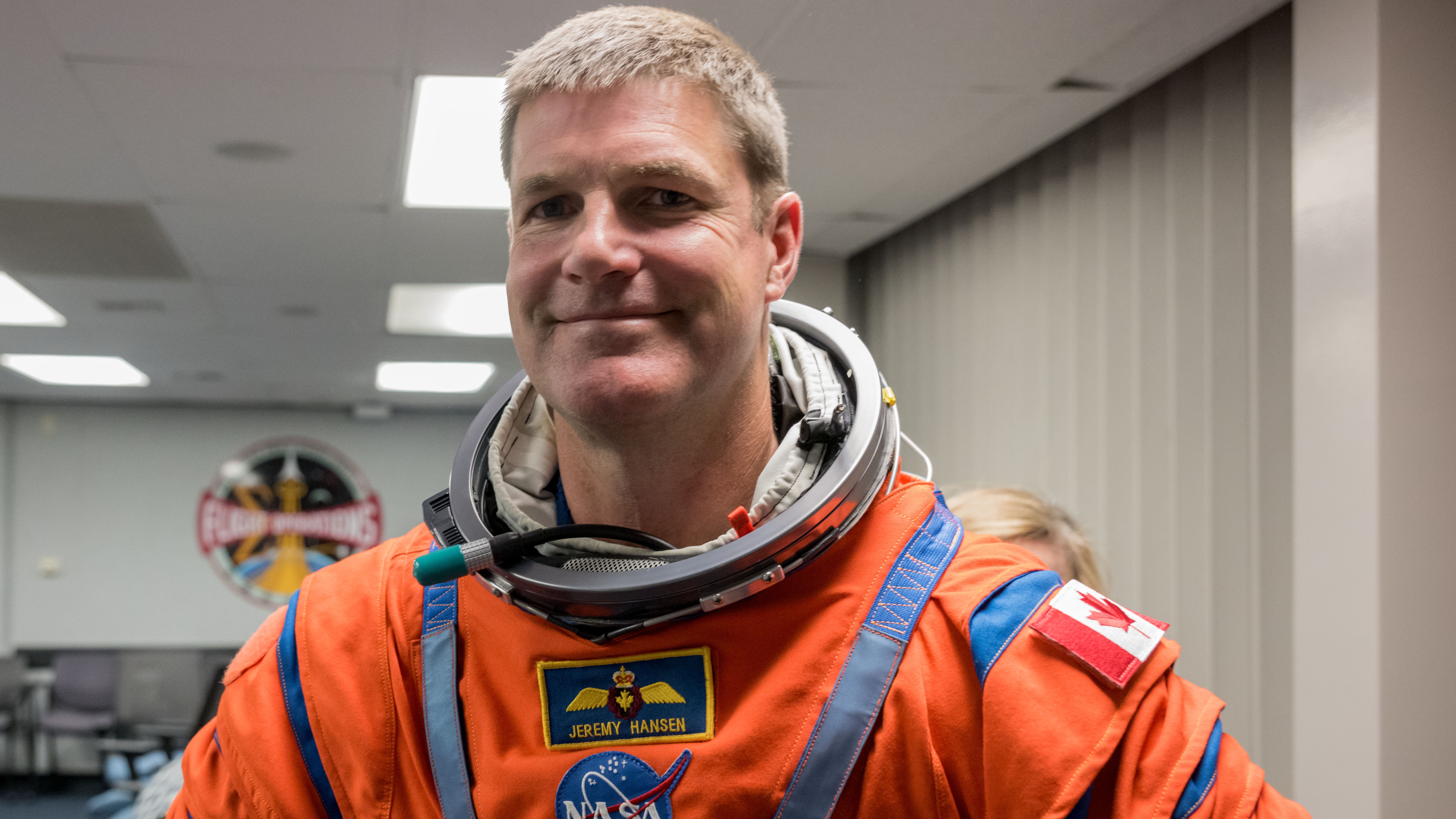 Jeremy Hanson smiles in orange spacesuit at NASA facility