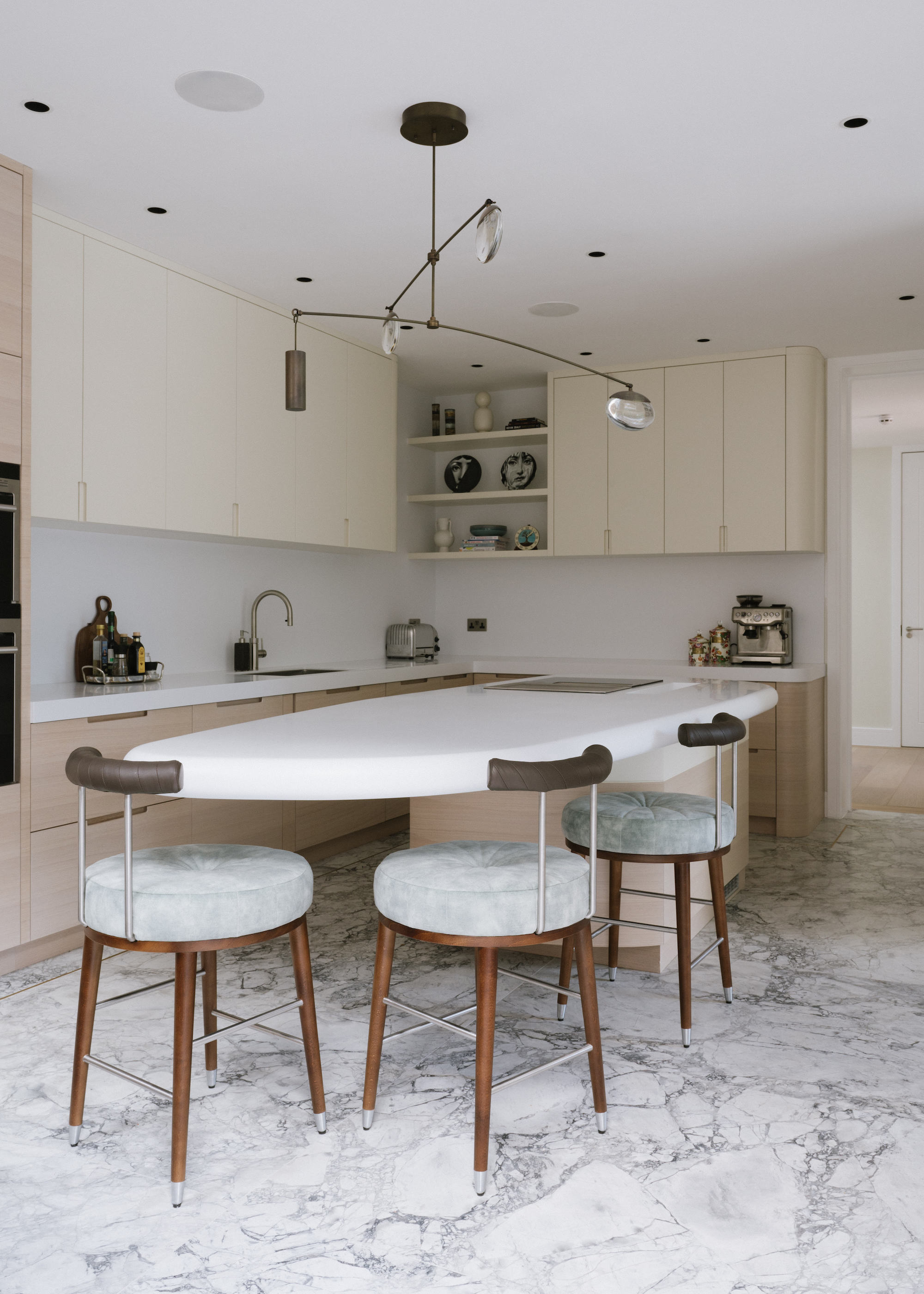 kitchen with white island with seating and a marble floor. there's a sculptural pendant above the island