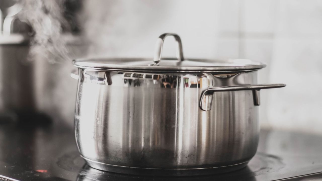 A stainless steel pot with lid on a flat stove