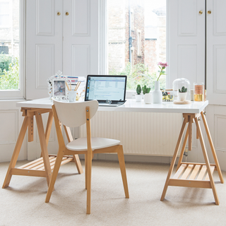 Laptop on workbench style wooden desk with white top and chair looking out of bay window in bedroom come home office.