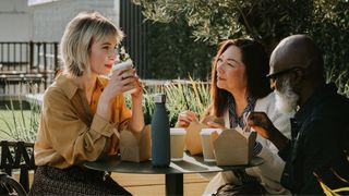 Two women and one man drinking coffee together outdoors in the sunshine