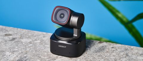 a small PTZ webcam with 4K resolution and a magnetic attachment clip is photographed in front of a blue background and a green plant