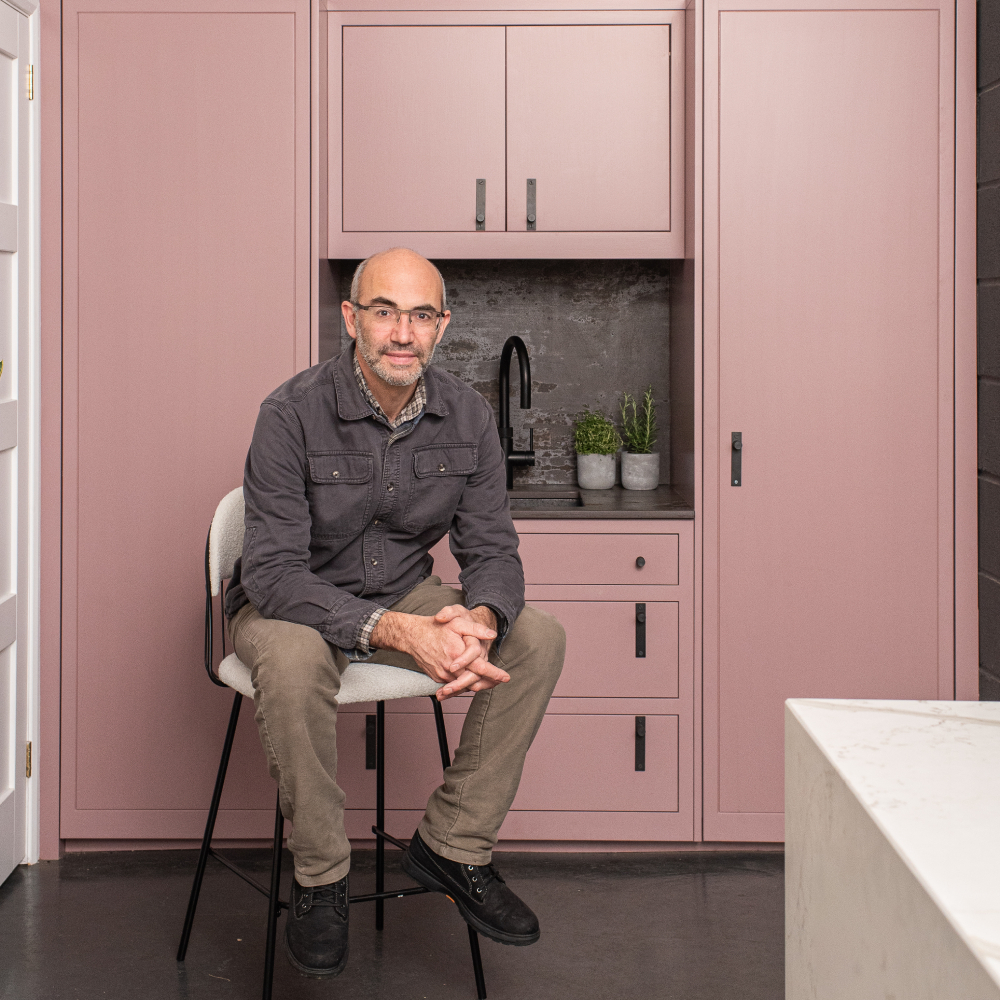 male sat on stool in front of pink kitchen cabinets