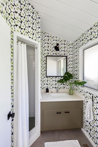 A bathroom fully wallpapered with a small shower section, covered with a curtain