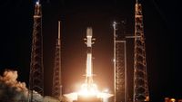 a white and black rocket lifts off into the darkness of night, its bright orange-tinted plume lighting up its launch pad.