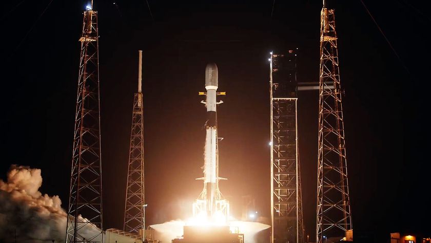a white and black rocket lifts off into the darkness of night, its bright orange-tinted plume lighting up its launch pad.