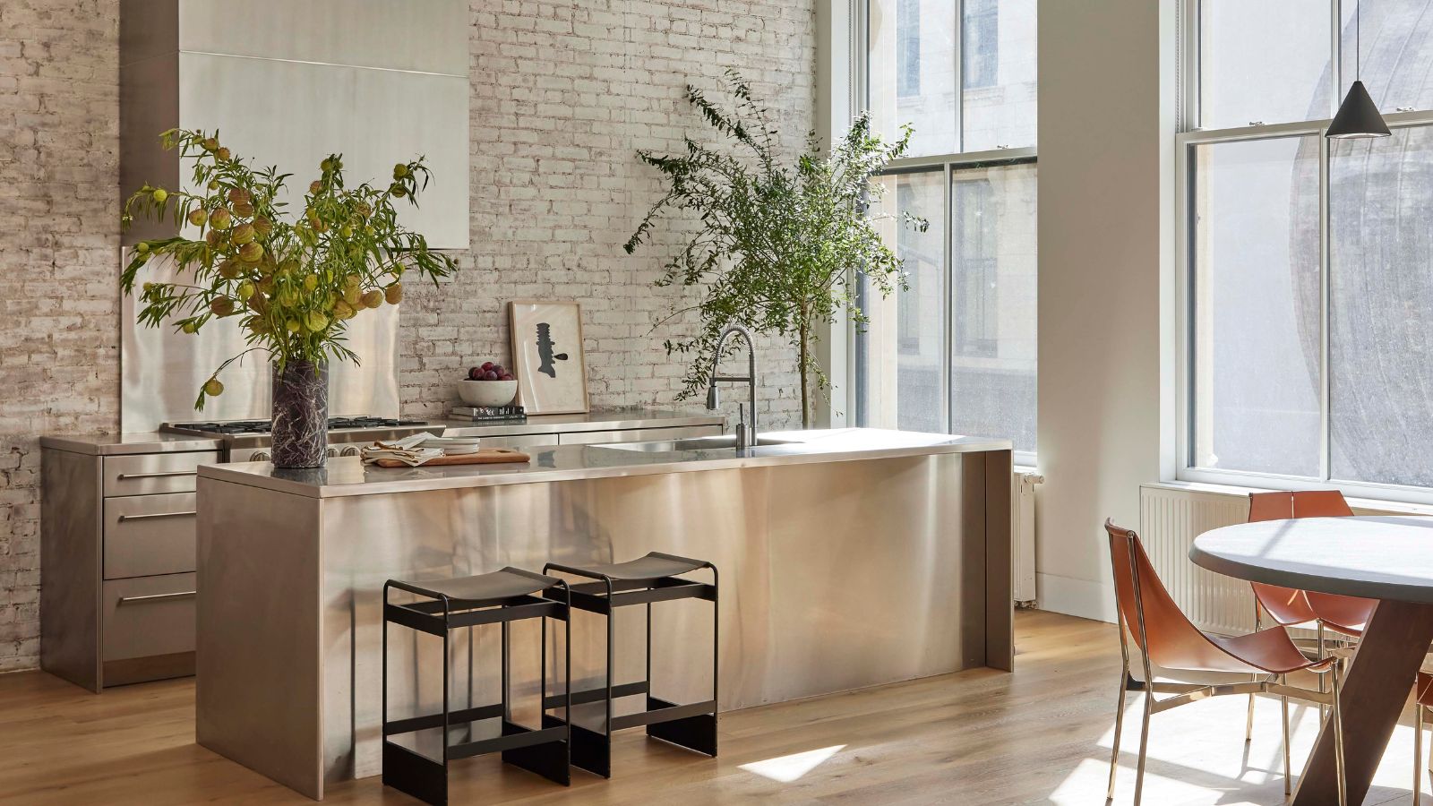 An open plan stainless steel kitchen with an island and vases filled with seasonal greenery
