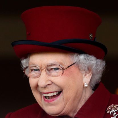 Queen Elizabeth wearing a maroon hat and coat laughing