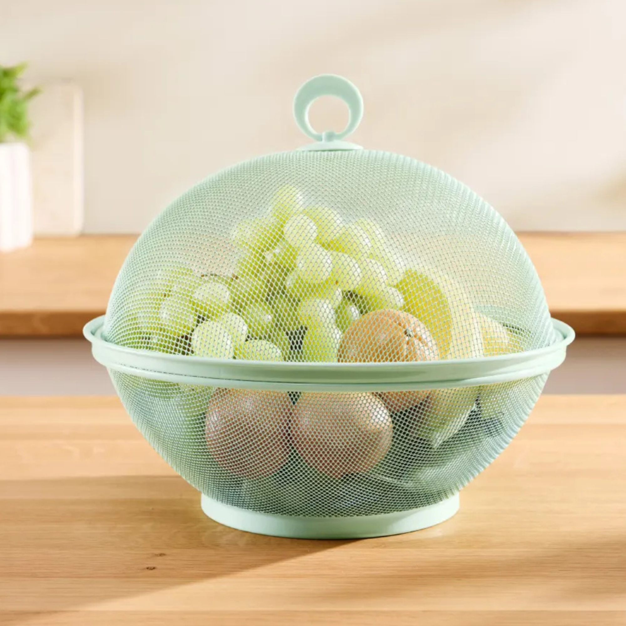 Lidl green metal mesh fruit bowl on wood worktop.