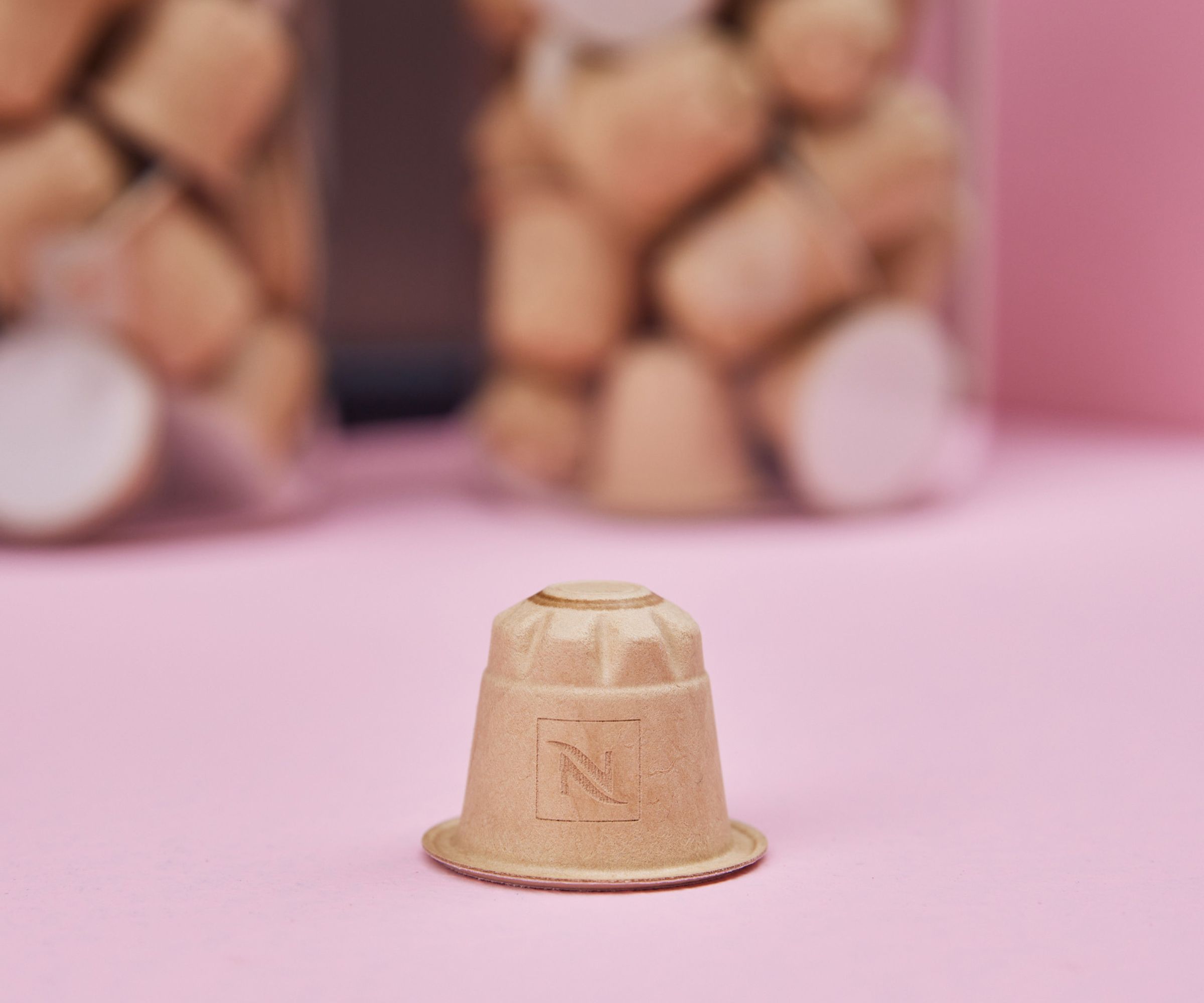 Nespresso paper coffee pod  on a pink surface with jars of coffee pods in the background