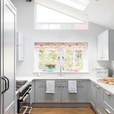 grey galley kitchen with a pink floral blind, skylight and wooden flooring