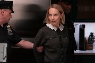 Amy Ryan as Jan (center) stands in a kitchen with her hands behind her back, as a police officer (left) grabs her arm, in 'Only Murders in the Building' season 4.