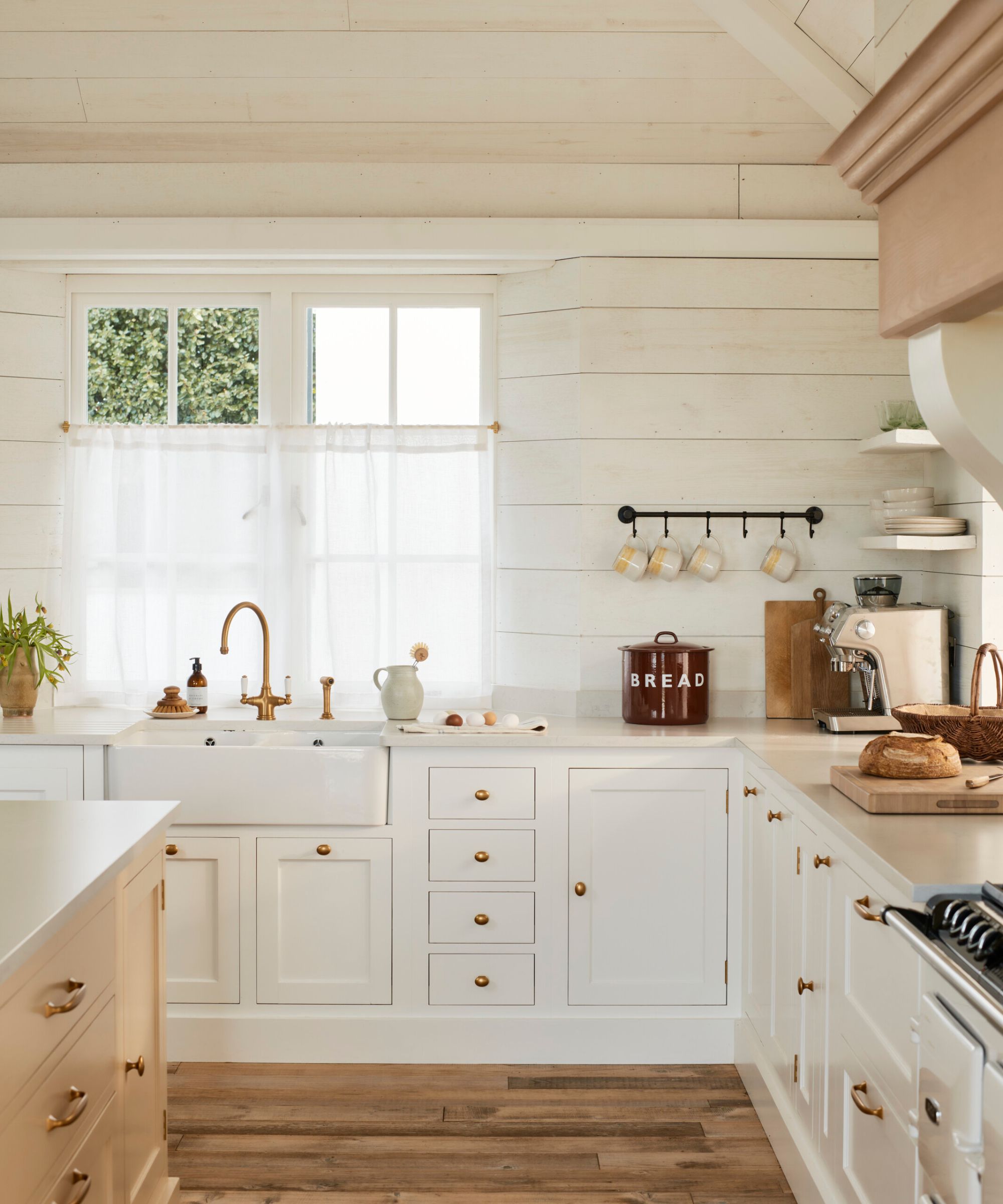 A coastal kitchen with white wall paneling, warm white cabinets, and a wood island