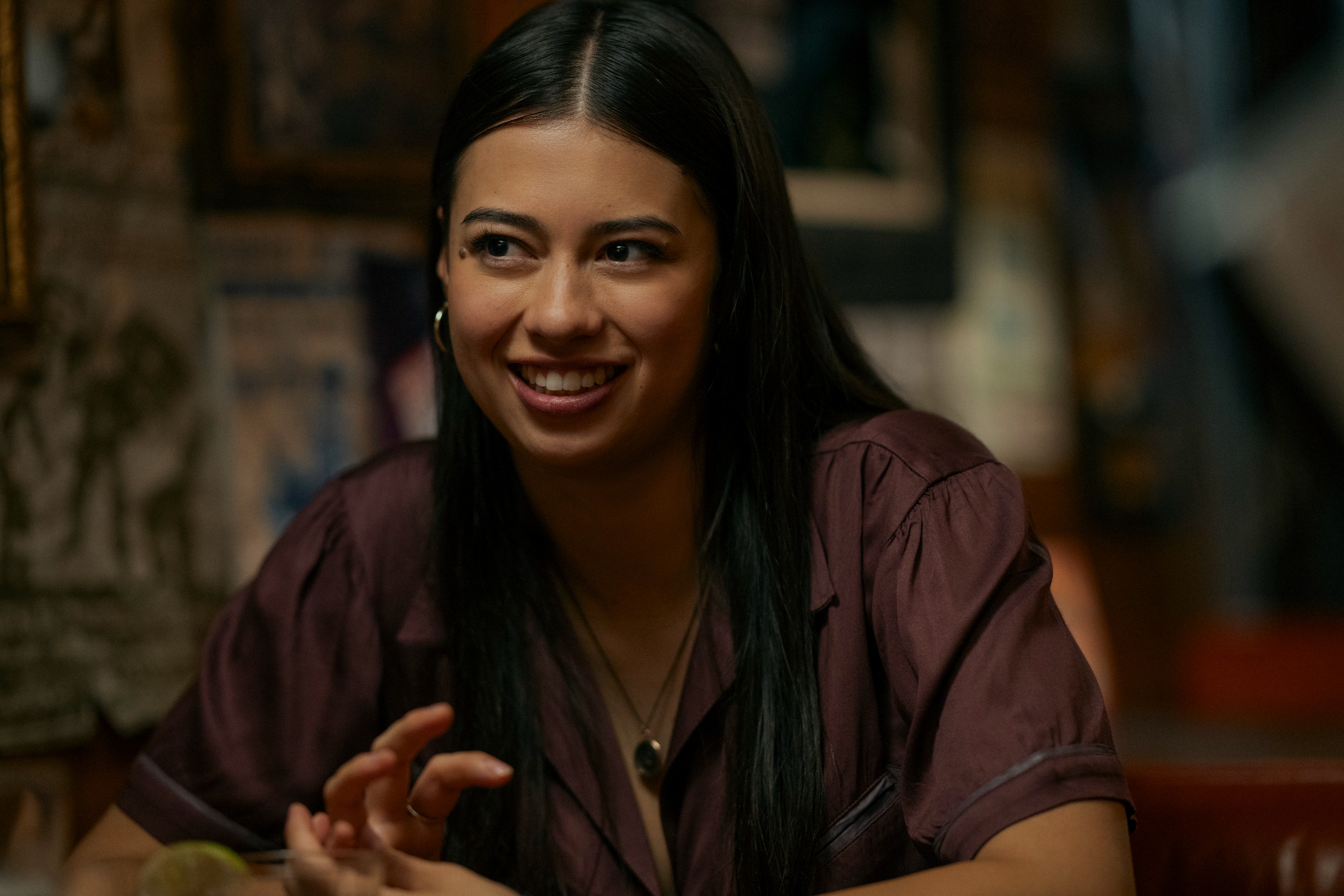 A woman in a brown blouse (Amber Midthunder as Rita Desjardin) sits at a bar booth, in Prime Video's 'Carrie.'
