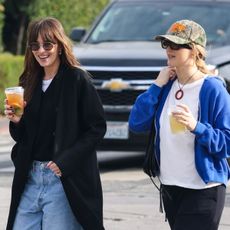 Dakota Johnson wore round sunglasses, a black sweater, white t-shirt, black coat; Jennifer Lawrence wears a camo hat, oversize sunglasses, a white t-shirt, pendant necklace, blue zip-up sweatshirt, and black sweatpants.