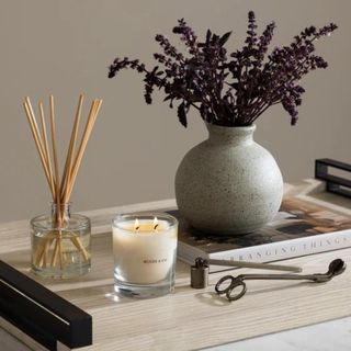 A coffee table with a vase of flowers, diffuser, candle and coffee table book