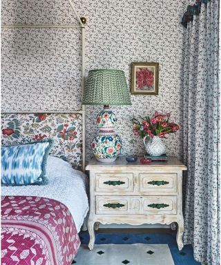 bedroom with patterned wallpaper and headboard and bedding and wooden bedstand with patterned lamp