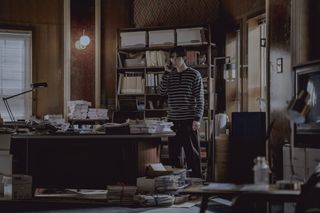 Park Seo-jun as Jang Ho-jae, talking on a cell phone as he stands in an office covered in piles of papers, in Gyeongseong Creature S2.