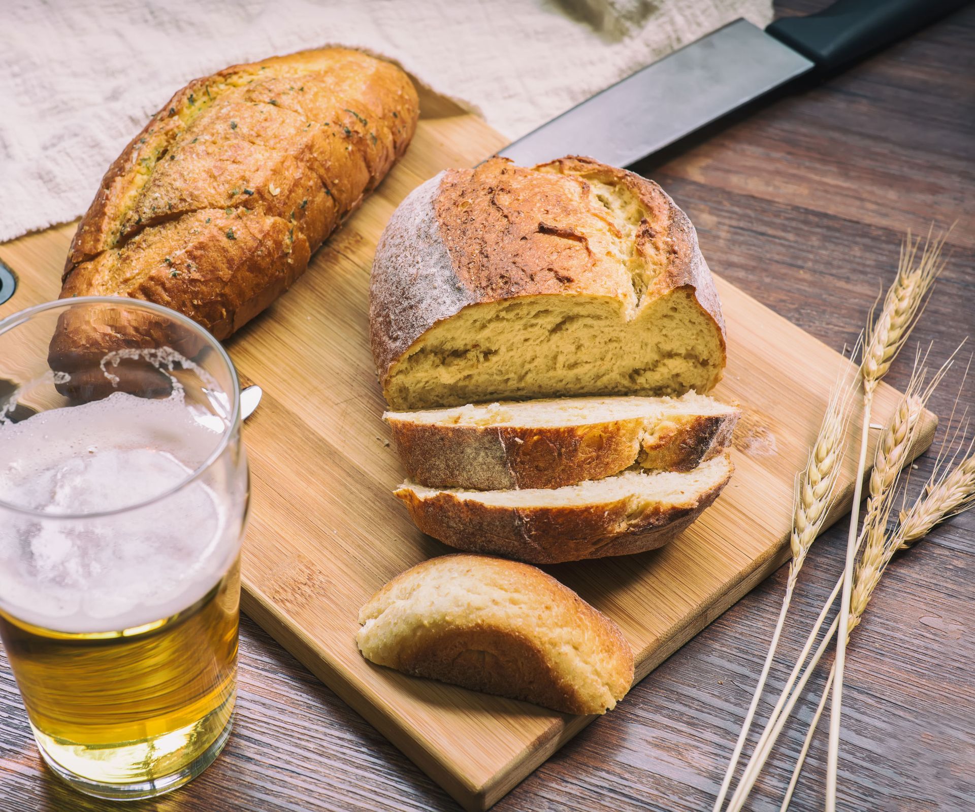 sourdough bread and beer on wooden table and chopping board with wheat and knife