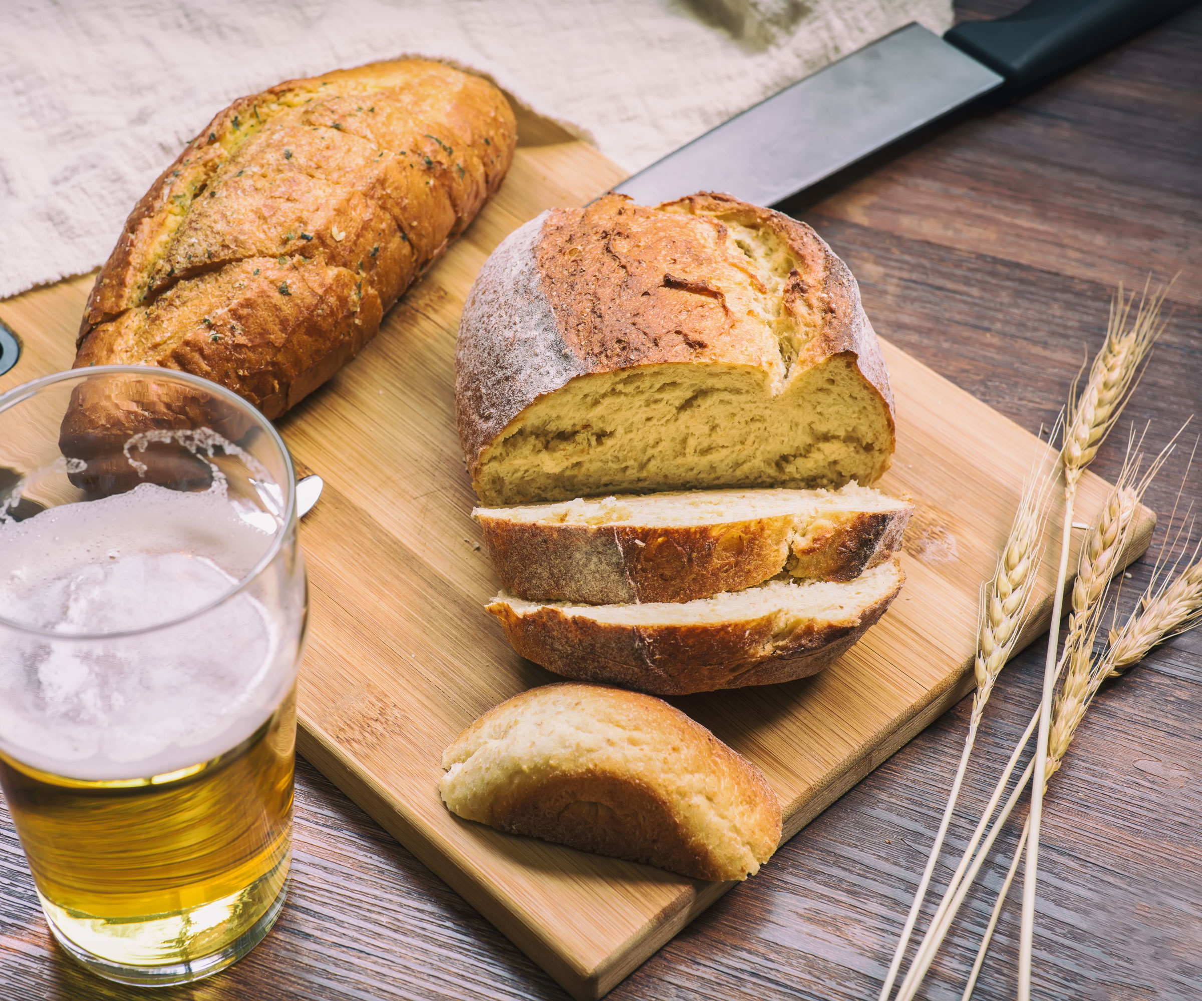 sourdough bread and beer on wooden table and chopping board with wheat and knife