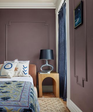 bedroom with muted purple walls, white ceiling, bed with blue patterned bedding and wooden nightstand with dark blue lamp