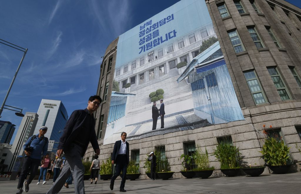 Pedestrians walk past a giant banner showing a picture of the summit handshake between South Korean President Moon Jae-in and North Korean leader Kim Jong Un.