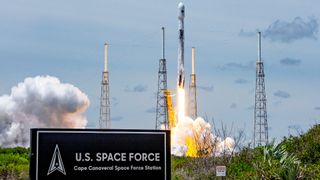 A SpaceX rocket lifts off in the background behind the sign for Cape Canaveral Space Force Station