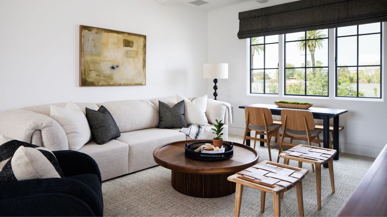 living room with white walls, white sofa, desk , wood round coffee table and two stools