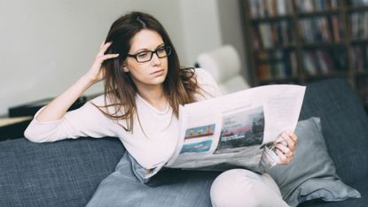 Woman sitting on couch reading newspaper