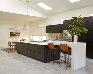 Large kitchen-diner space with vaulted ceiling with skylights, large kitchen island with seating, hanging pendants, gray stone flooring, black kitchen cabinets