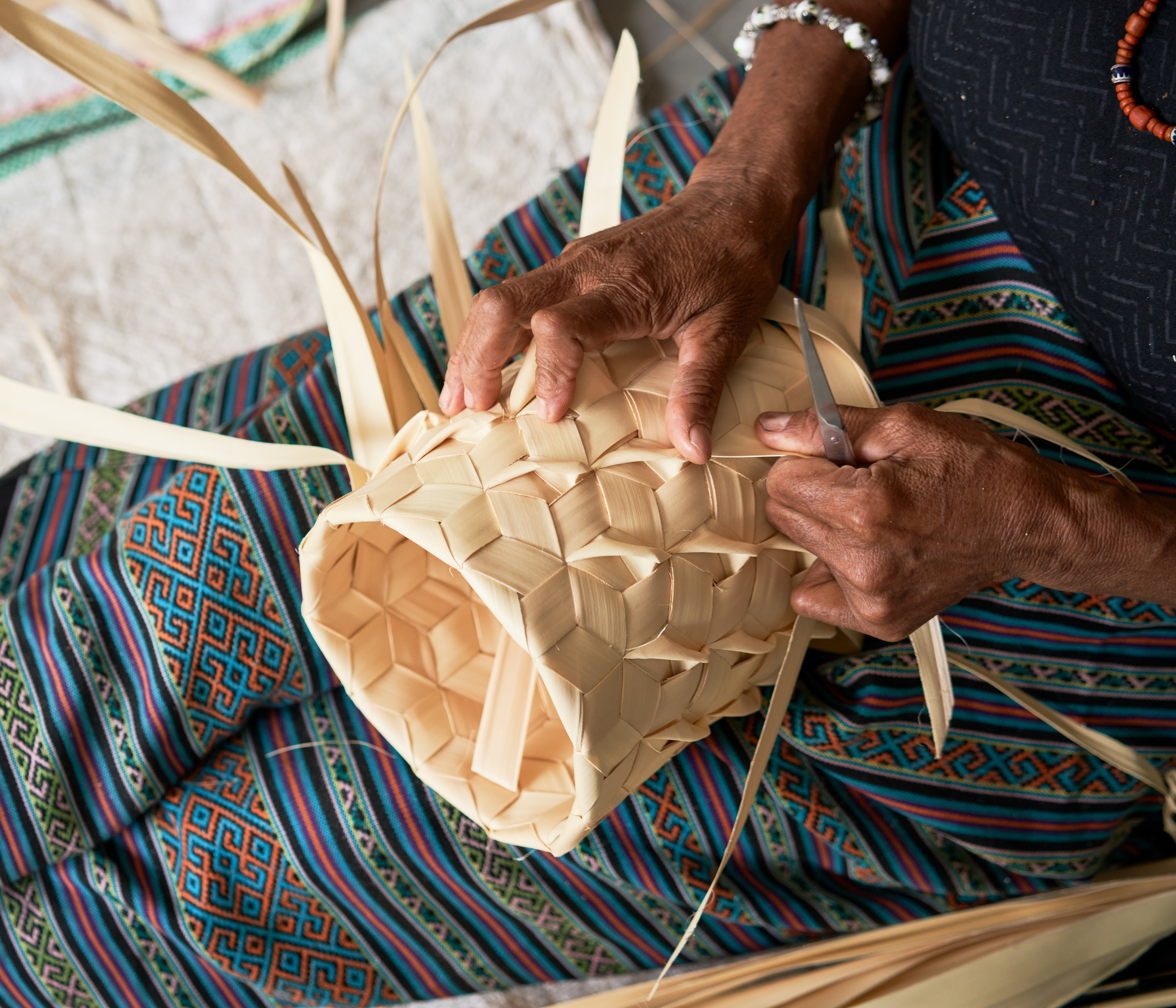 Hands shown working with palm fibre to weave a basket