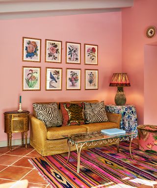 coral/pink living room with gold couch, artwork, gold side table, lamp, multicoloured rug