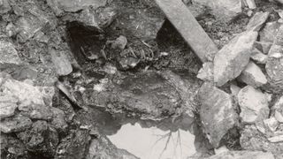 a black and white photo showing a skeleton scattered among rocks, dirt, and water