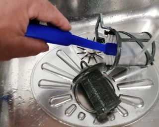 A dishwasher filter being cleaned with a brush