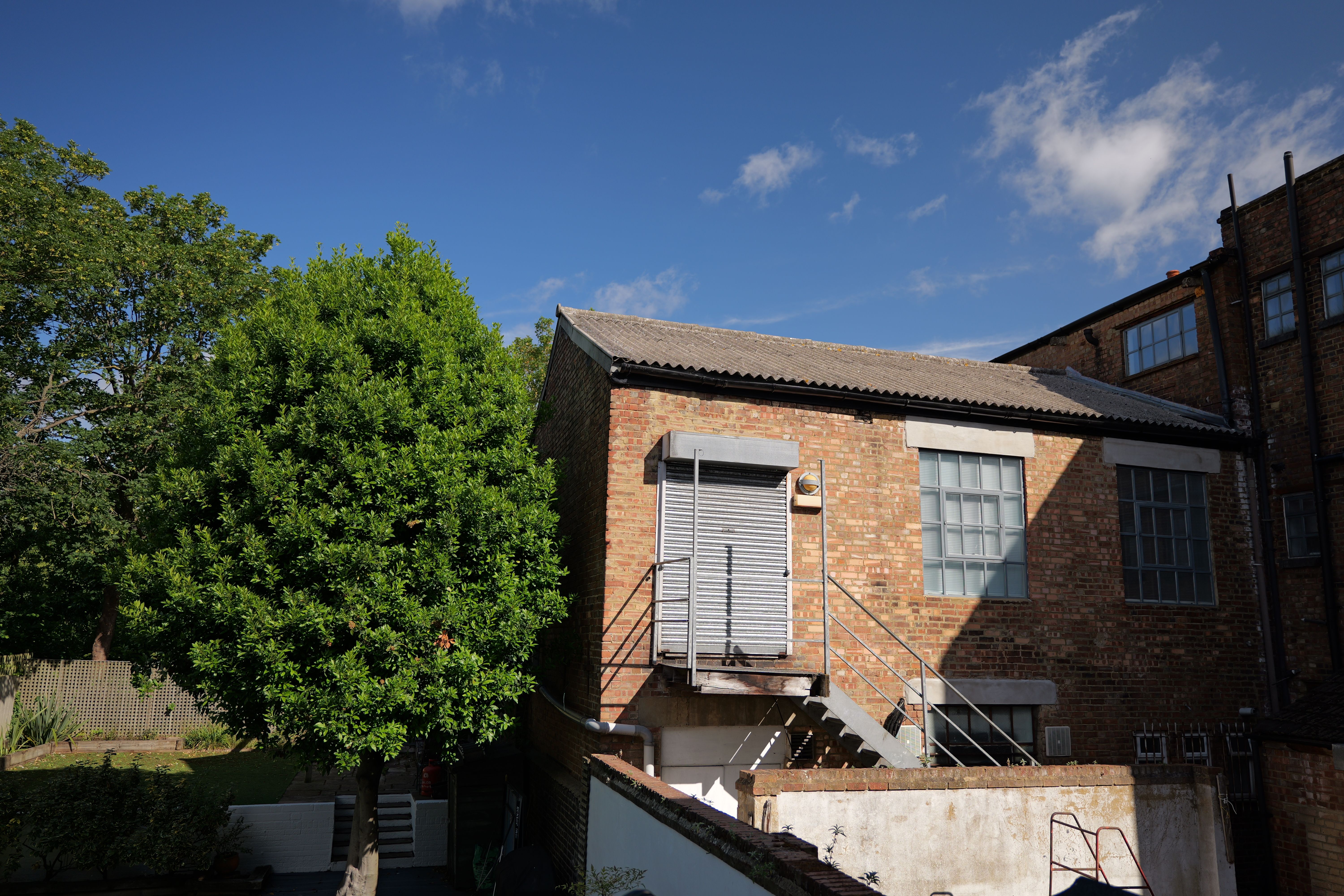 A warehouse next to a tree in front of a bright blue sky