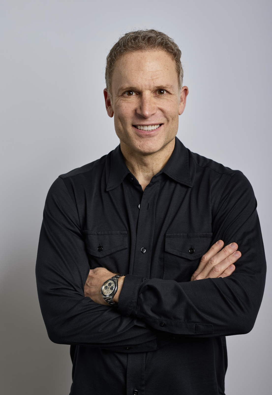 a headshot of a man wearing a black button down shirt in front of a gray background