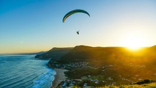 A paraglider mid-air, flying over Stanwell Tops in Australia