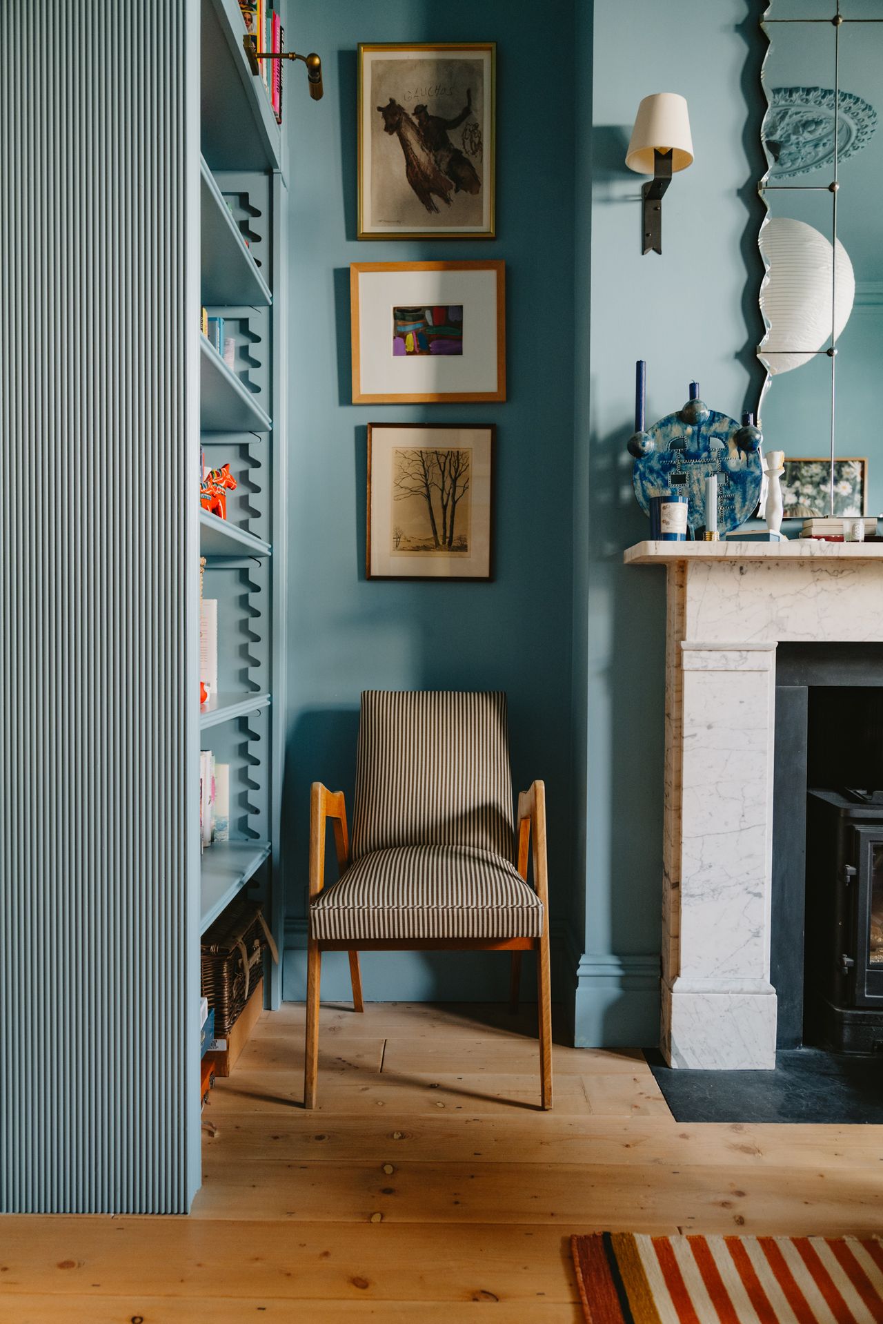 Image of a wooden and striped chair in a light blue room next to a built-in bookcase and a white fireplace.