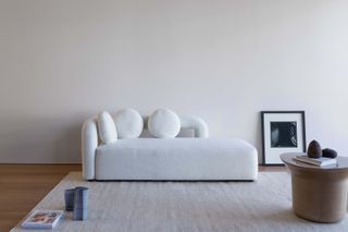 minimalist white sofa in white room, with black & white artwork on the floor leaning on the wall