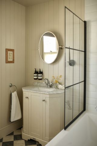 A neutrally decorated bathroom with wood panelled walls, a marble sink countertop, and a black bath screen