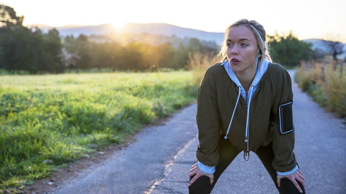 Young woman outdoors, taking a break from exercising, hands on knees