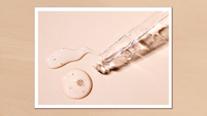 A close up of a glass pipette with drops of clear serum-like liquid on a beige backdrop/ in a beige, textured template 